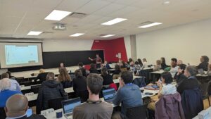 Une salle d’étude où une vingtaine de personnes sont assises, avec une image projetée sur un écran.